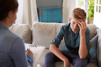 a teen puts their fingers on their forehead during psychotherapy for adolescents