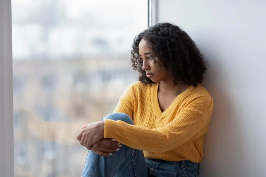 Woman leans against wall, looks out window and wonders what is seasonal affective disorder