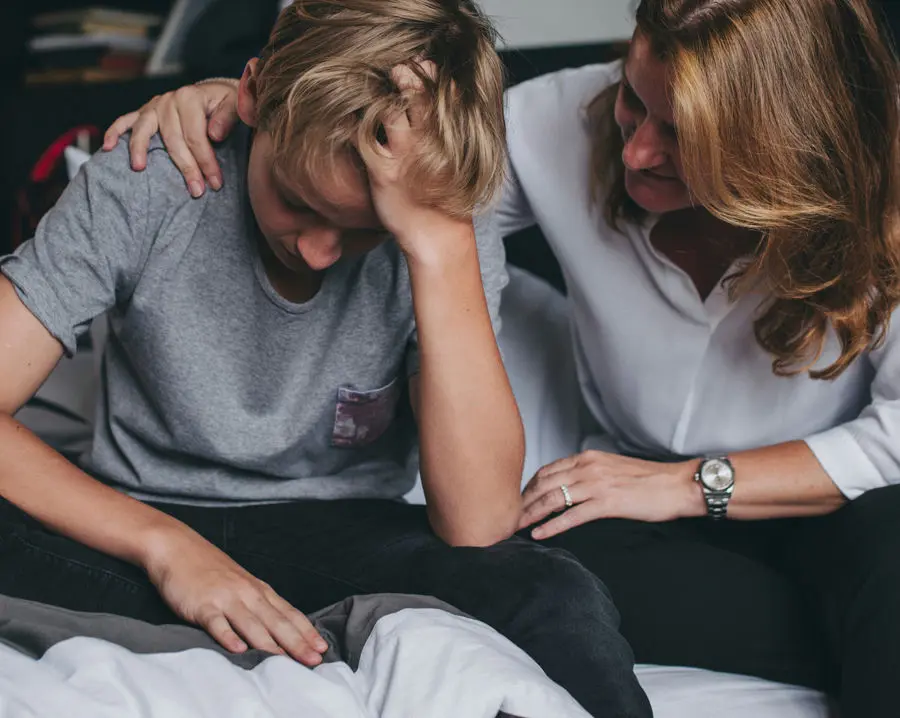 Parent talking with their teenager in a bedroom setting, watching for signs of bullying and emotional distress.