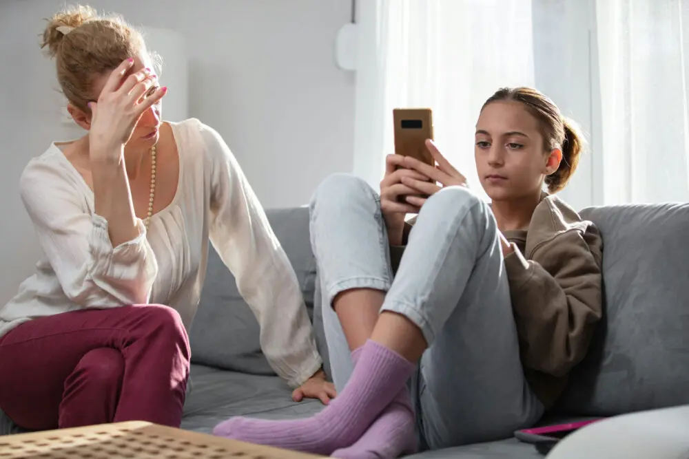 Teenage girl with ADHD and anxiety looking at smartphone next to frustrated woman.