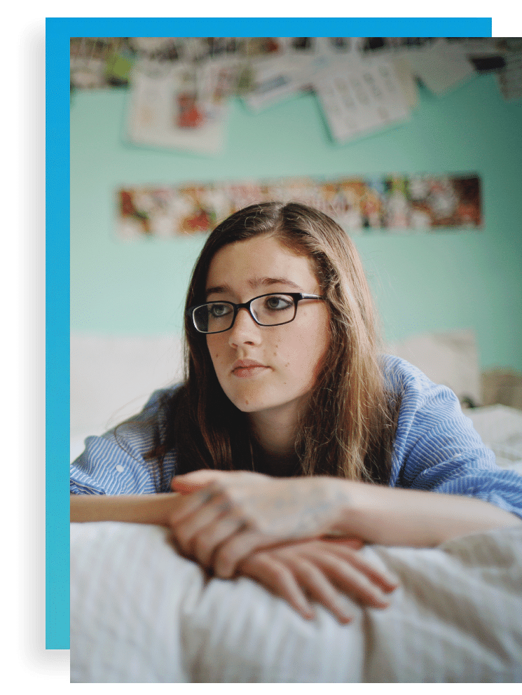 teen girl with glasses laying on bed with her hands crossed looking somber