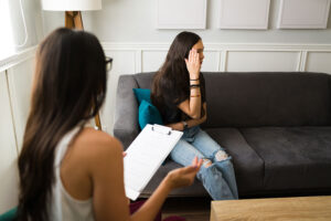 a teen covers their face while talking to a therapist during self harm treatment