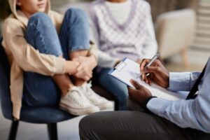 Teen curls up as they talk about family systems theory with parent and therapist