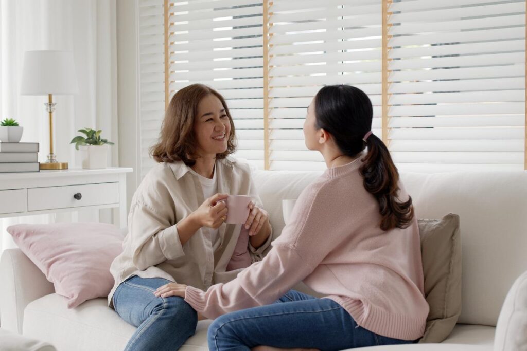 Woman sits on couch with her daughter after she returns from rehab for teens