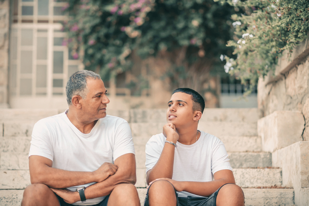 Father talks to son on steps about receiving guidance on how to get a teenager to talk about their feelings