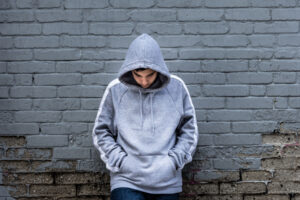 Teen in hoodie leans against wall as he considers school refusal