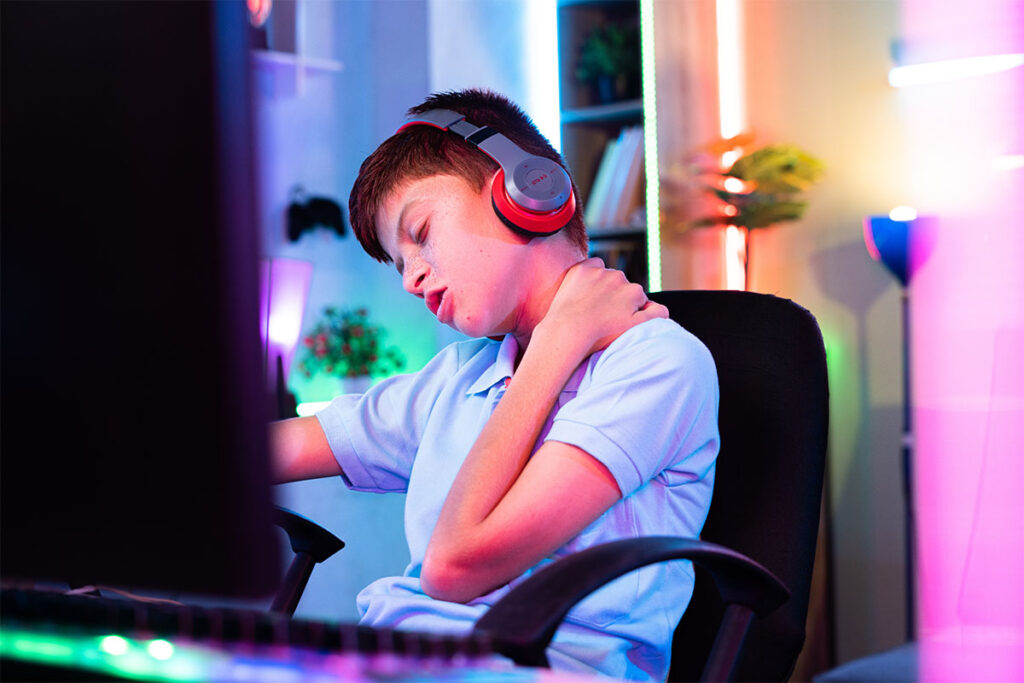 Teen with video game addiction sits in computer chair and tends to his sore neck
